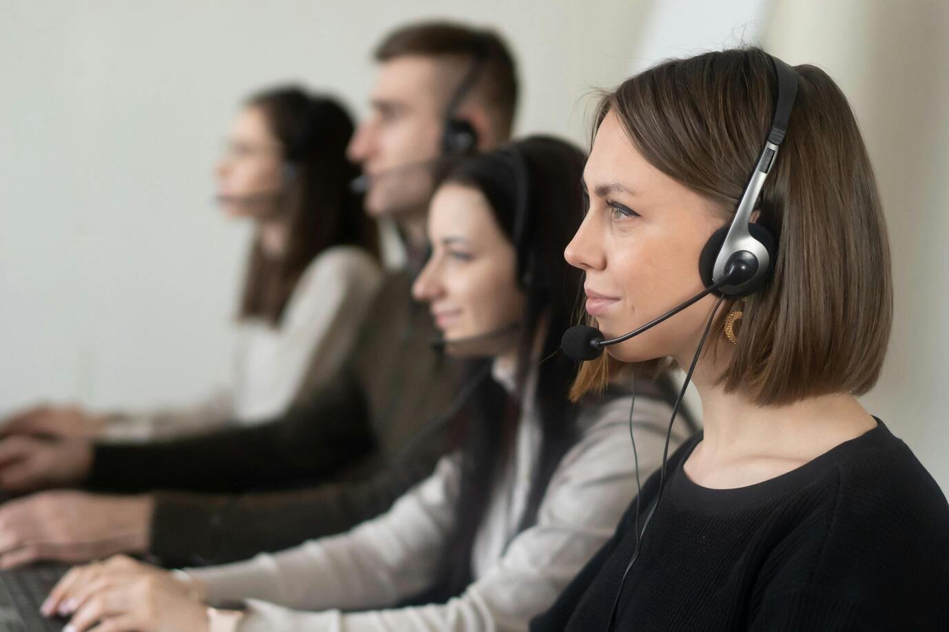 A group of women and men in a call center environment with telephone headphones and sitting in front of computers.