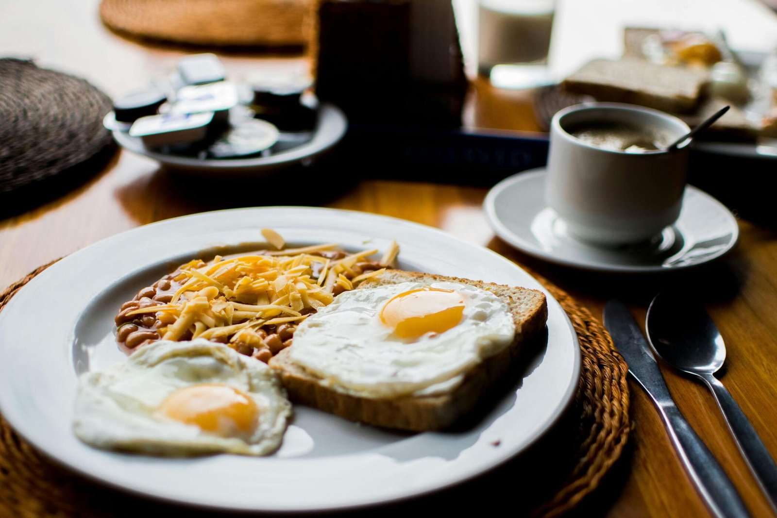 A plate of sunny side up eggs on toast and hashbrowns sits on a table beside a cup of coffee and silverware.