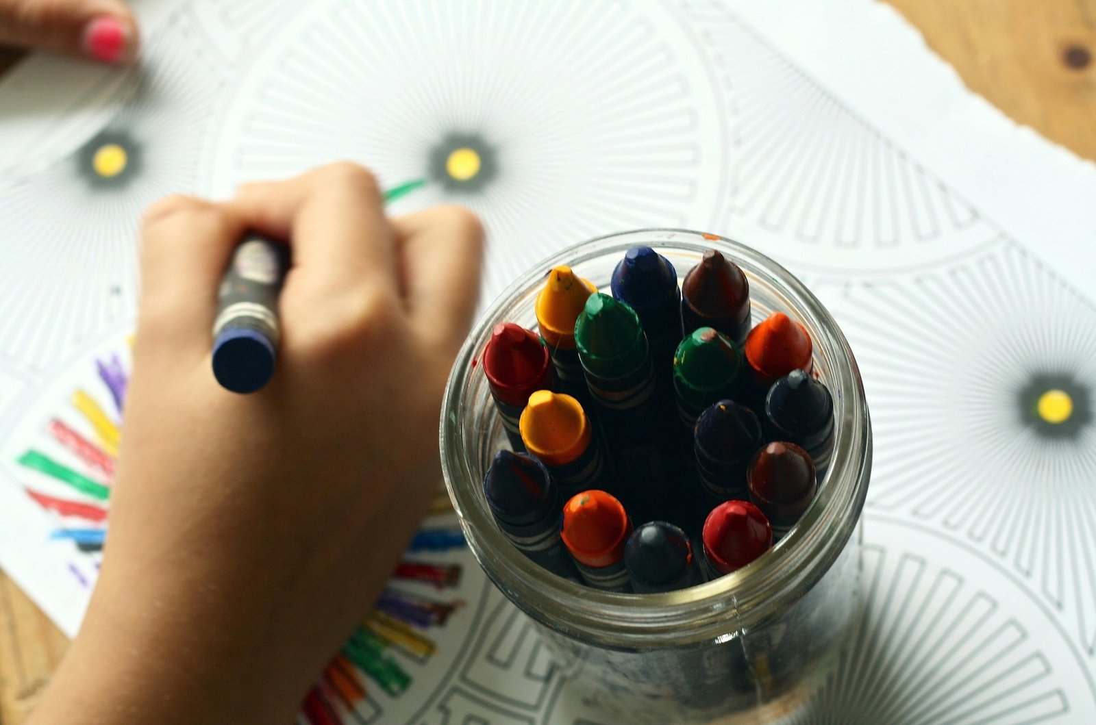 A child is coloring a picture with a bowl of berries next to them. The bowl contains a variety of berries, including blueberries, raspberries, and strawberries. The child is using a pencil to color the picture, and the bowl of berries is placed on a table. The scene is likely taking place in a home or a classroom setting, where the child is enjoying a creative activity while having a healthy snack nearby.