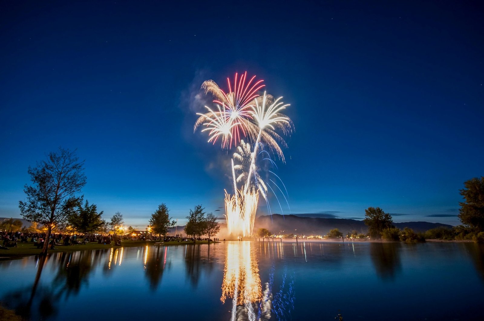 Vibrant fireworks bursting over a calm lake in the darkness.