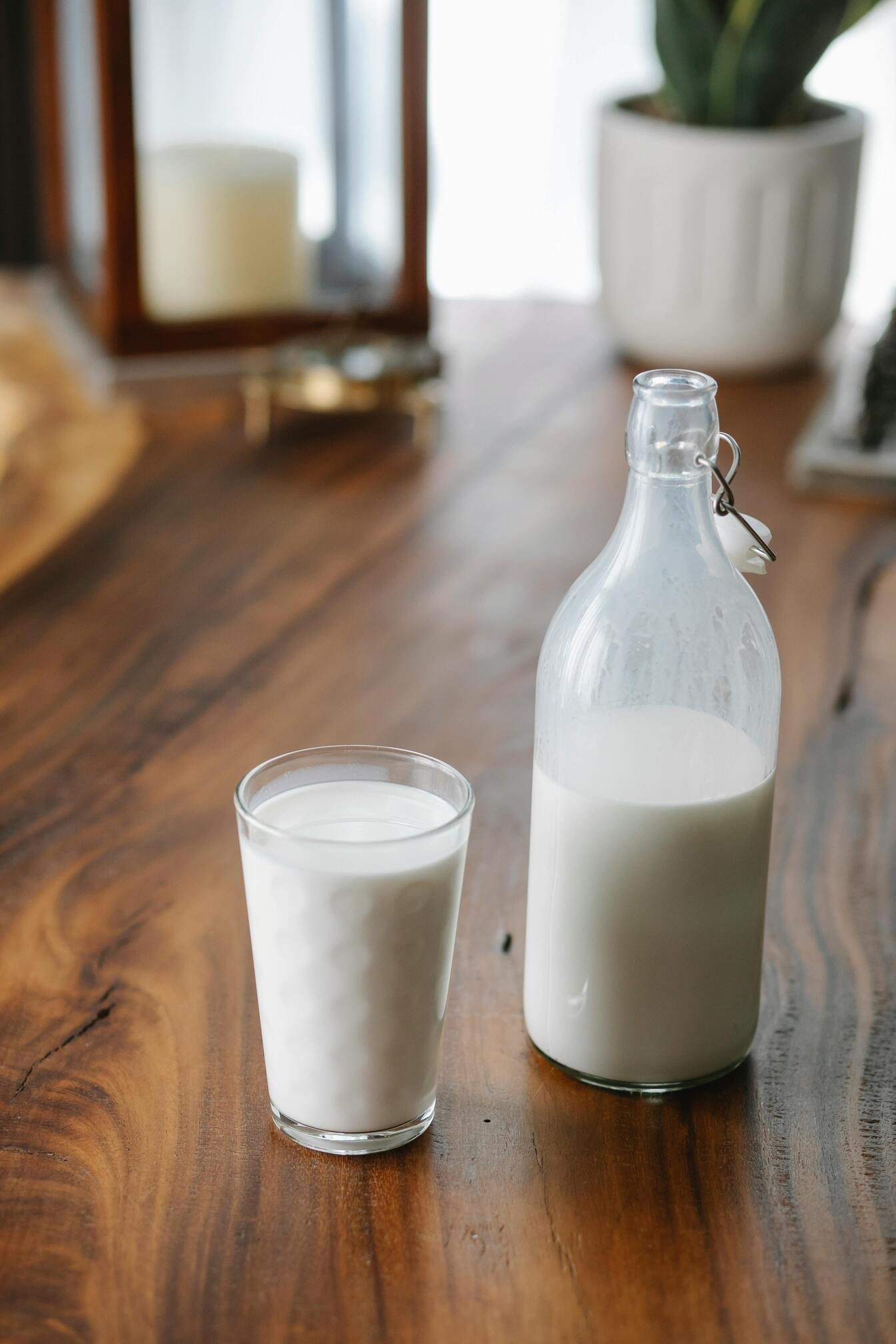 A glass bottle and a glass of milk on a wooden table.