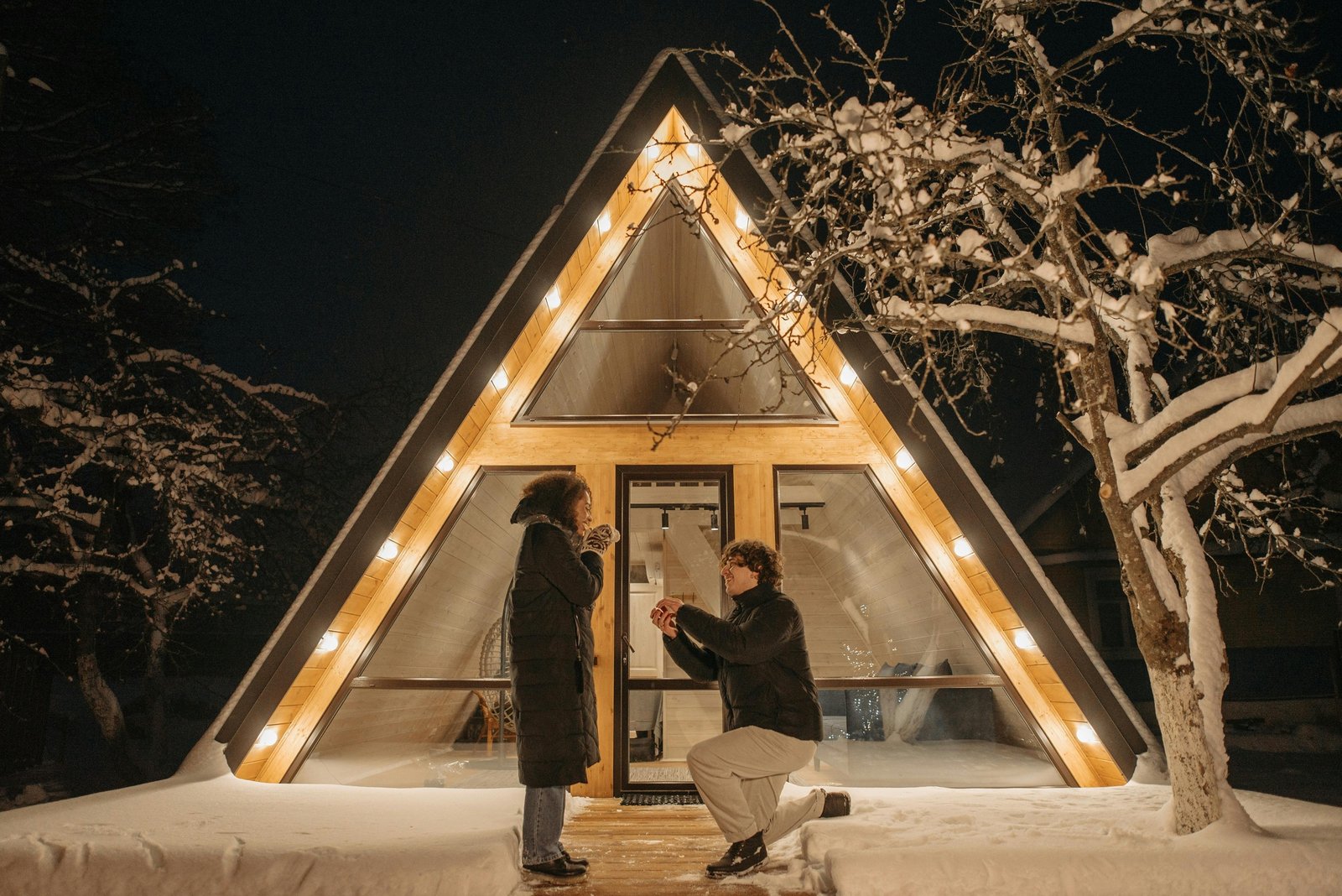 A nighttime proposal outside an illuminated A-frame cabin in winter.