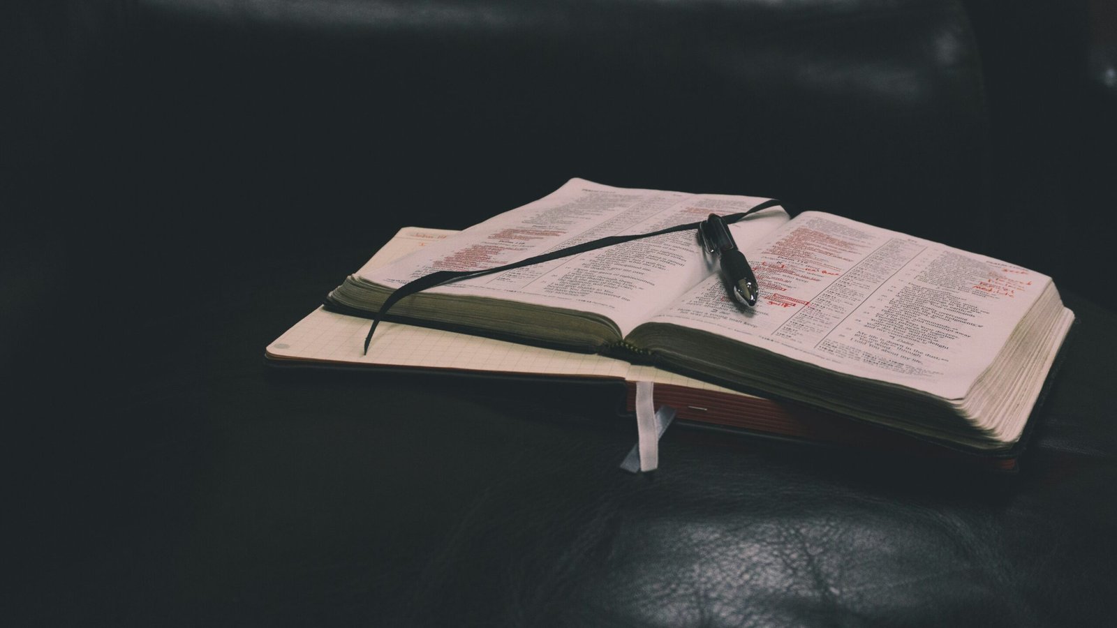 An open book with a pen resting on it, placed on a dark leather surface.